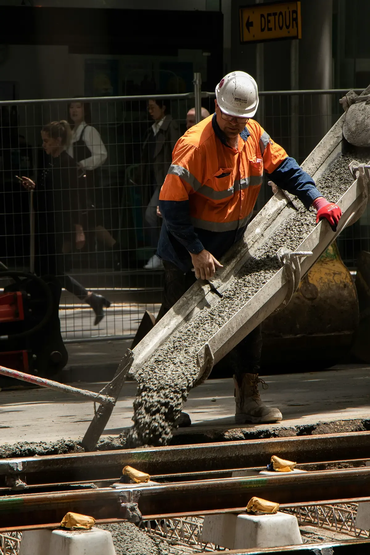 Bauarbeiter mit Schutzhelm und Warnkleidung verteilt Beton auf einer Baustelle